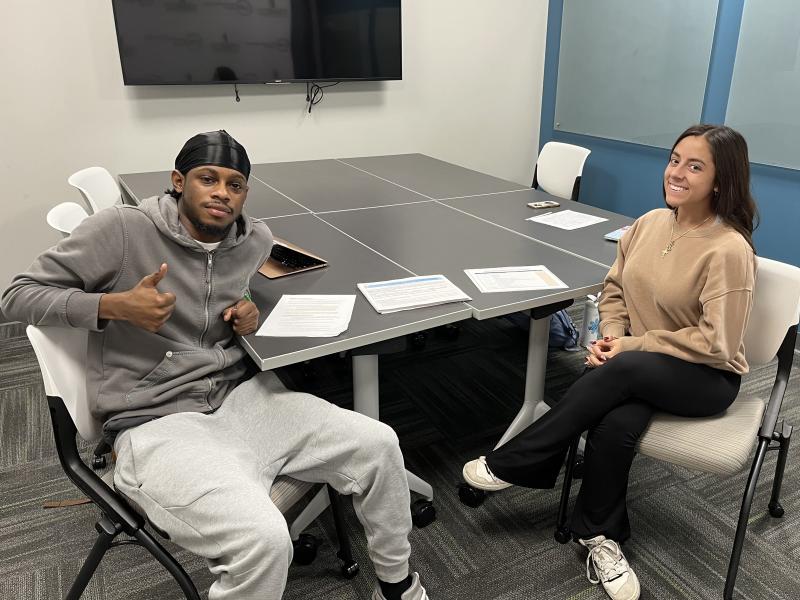 Two SUNY Oswego Empire State Service Corps students, Malik Hills and Izzy Ronacher, staff a walk-in session for students to apply for Supplemental Nutrition Assistance Program benefits in the Educational Opportunity Program Office in Penfield Library.