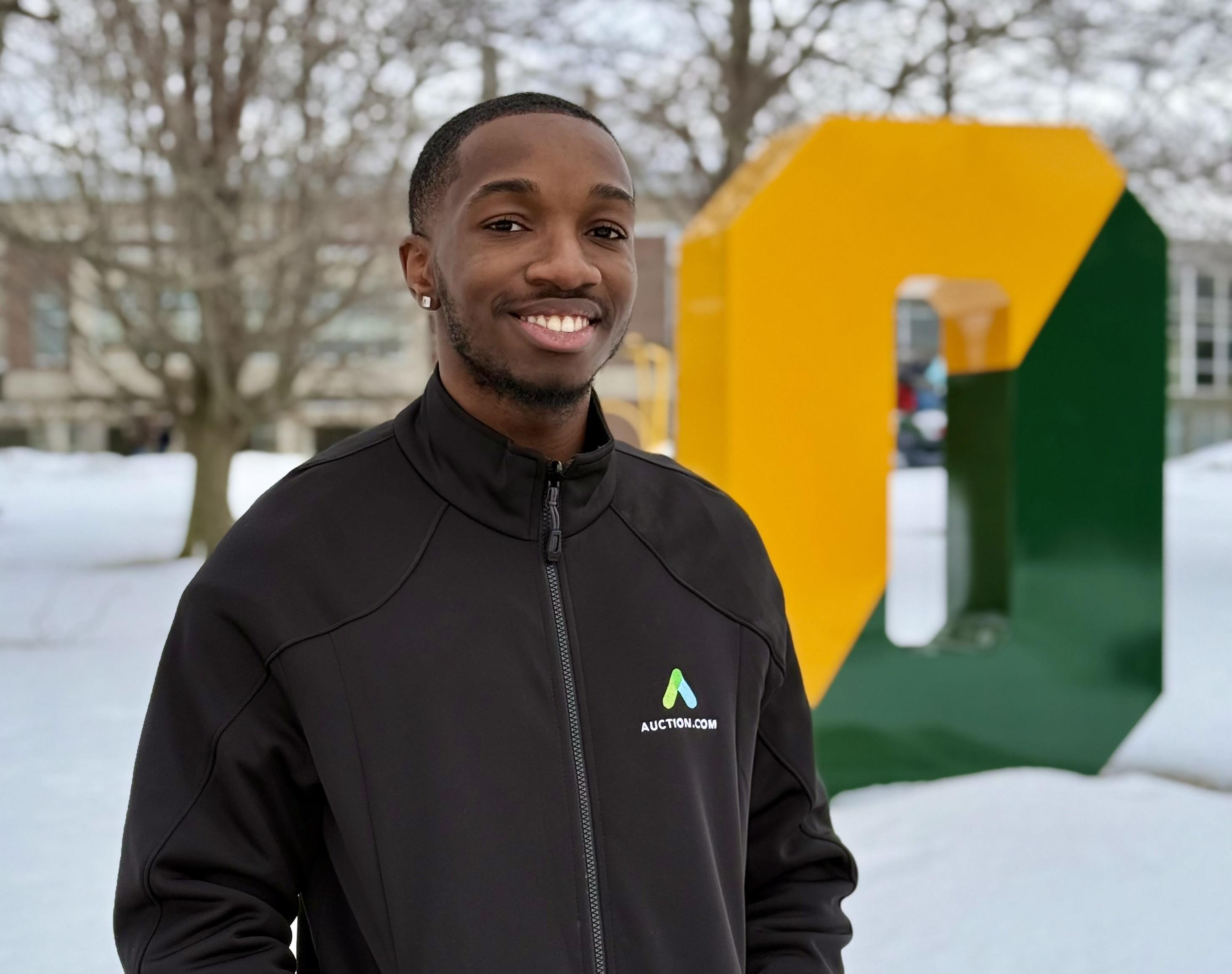 SUNY Oswego student Jaylen Cameron stands outside on campus in front of the Green and Gold "O."