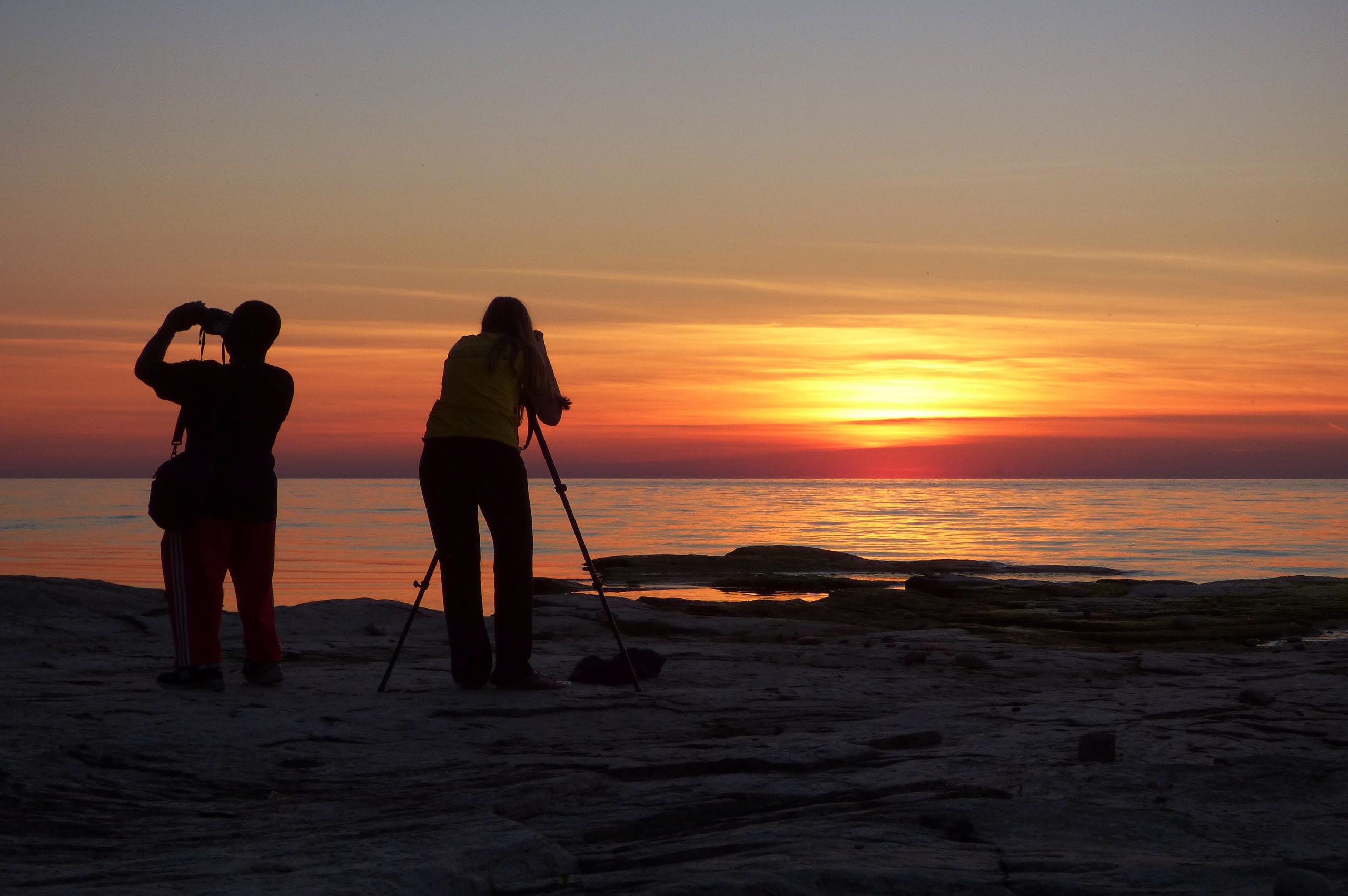 Two people take photographs on the shore of Lake Ontario