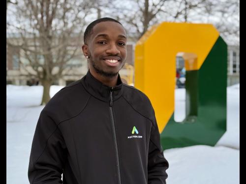 SUNY Oswego student Jaylen Cameron stands outside on campus in front of the Green and Gold "O."