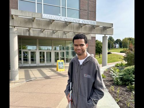 Student Luis Perez-Rivera stands outside in front of the Marano Campus Center wearing a grey hoodie.