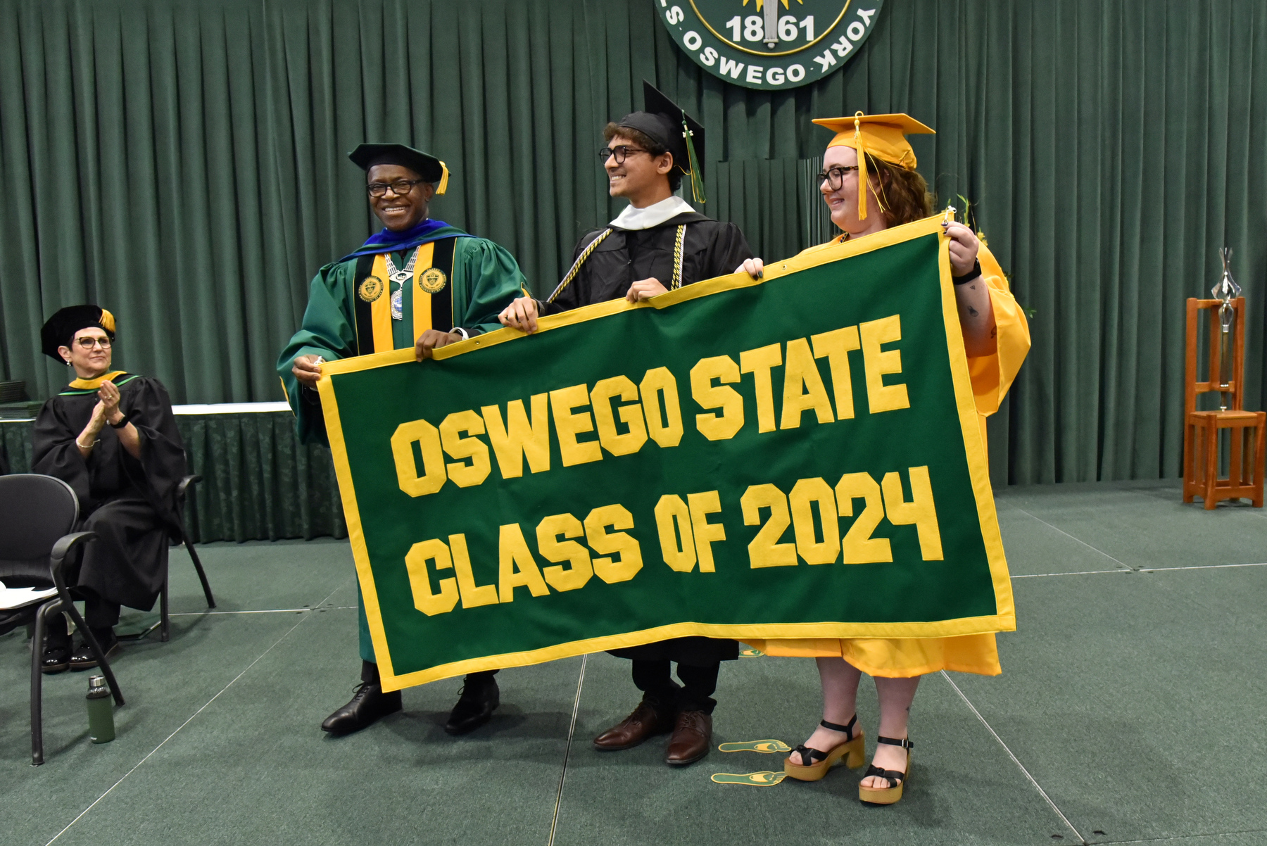 Mohammad Hammad and Amanda Streeter present the Class of 2024 alumni banner with President Peter O. Nwosu near the conclusion of the College of Liberal Arts and Sciences ceremony.