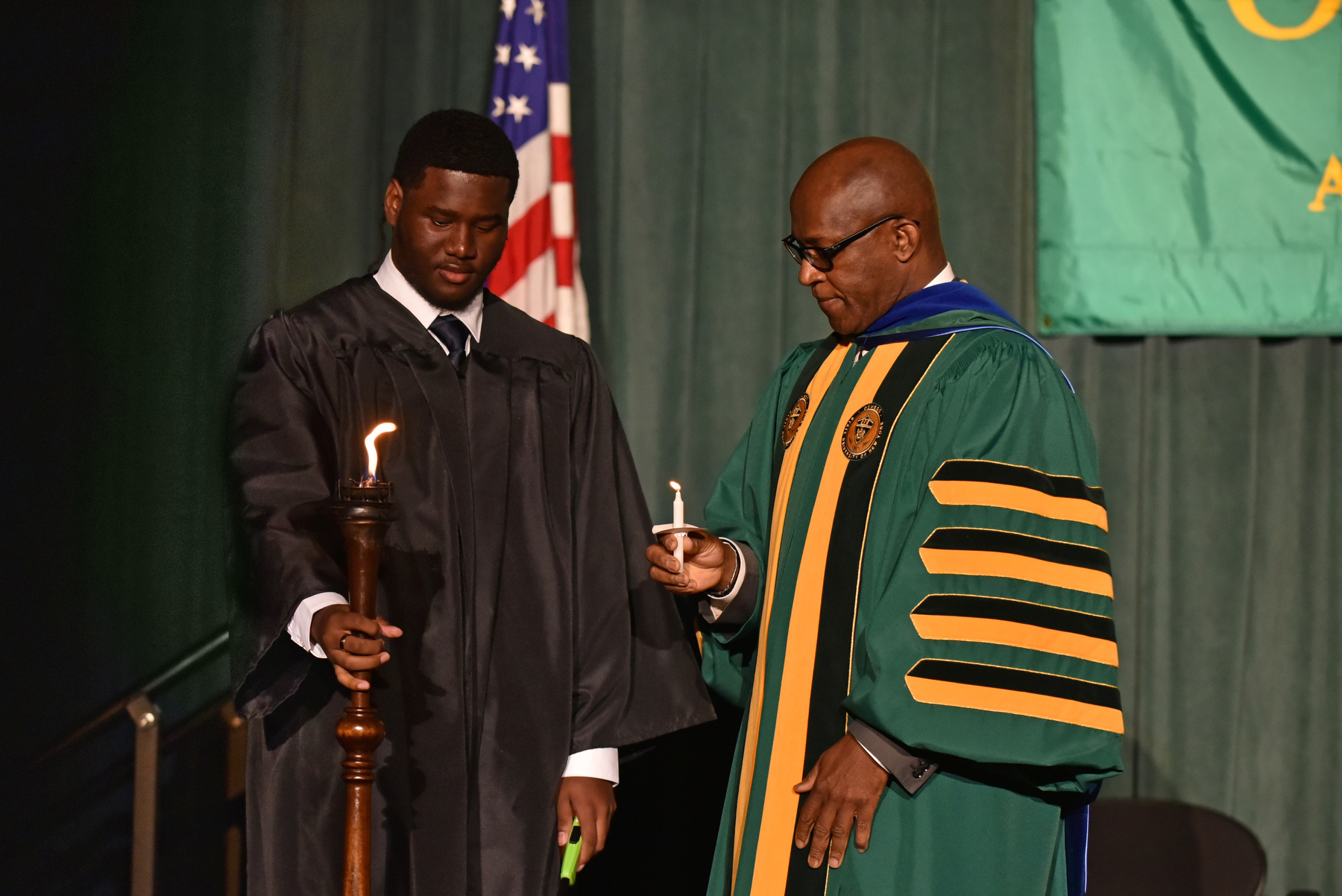 SUNY Oswego President Peter O. Nwosu lights his candle after Torchbearer and Student Association President Aiden Wilson lights the traditional torch on the platform during Welcoming Torchlight Ceremony on Aug. 21.