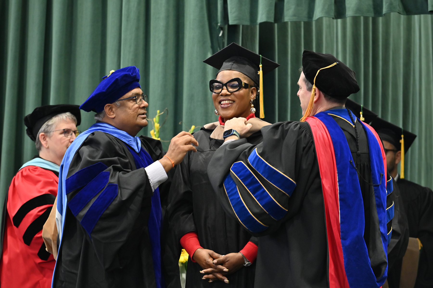 Jane Nwagu, an online MBA student from Nigeria who traveled to Oswego to attend Commencement, is bestowed with her master's degree hood by Prabakar Kothandaraman (left), dean for the School of Business, and Scott Furlong, provost and vice president for academic affairs, during the Dec. 14 Commencement ceremony. 