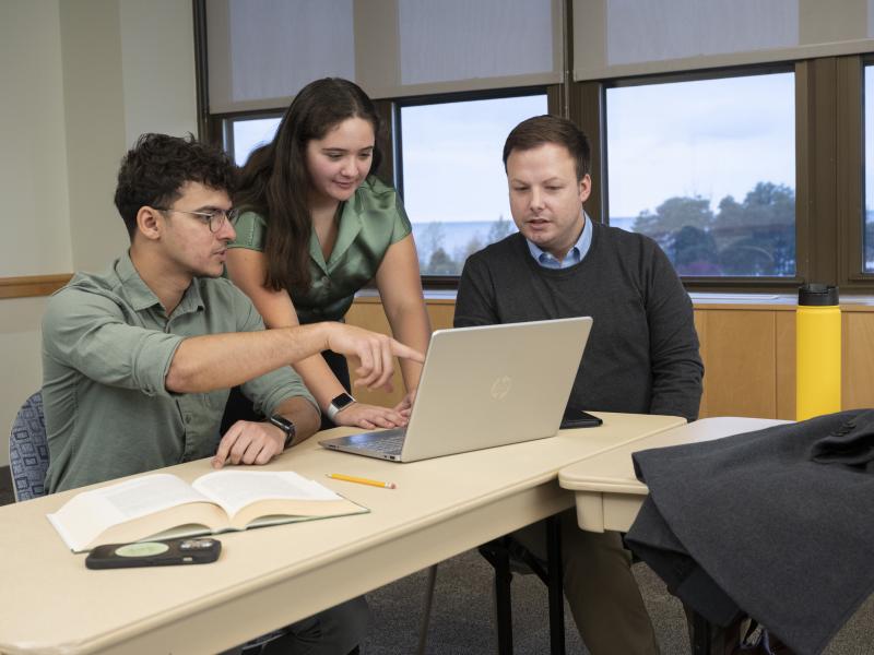 three graduate students working around a laptop