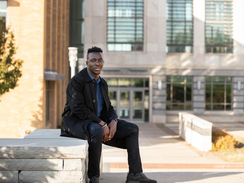 male student sitting on the wall outside the School of Education